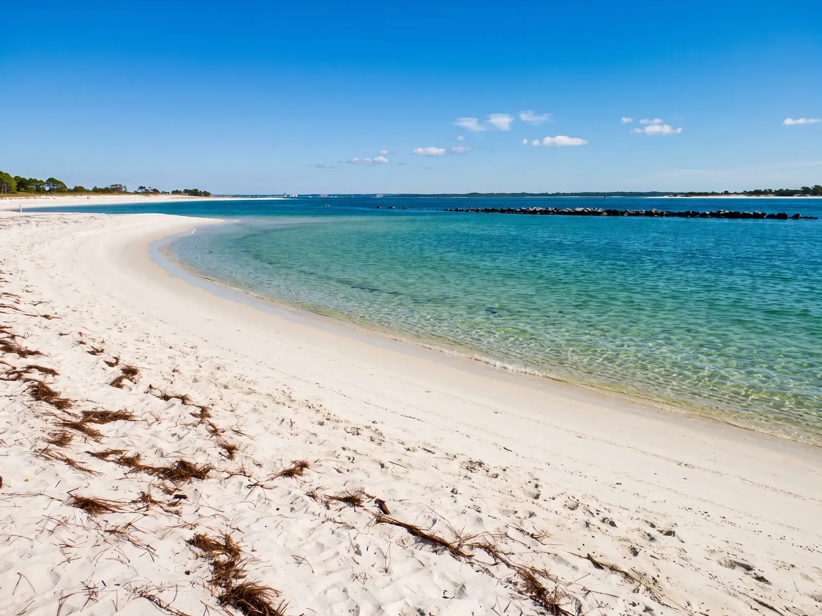 White sand and clear emerald-green water at St. Andrews State Park in Panama City Beach, on Florida's Emerald Coast, on a sunny day.